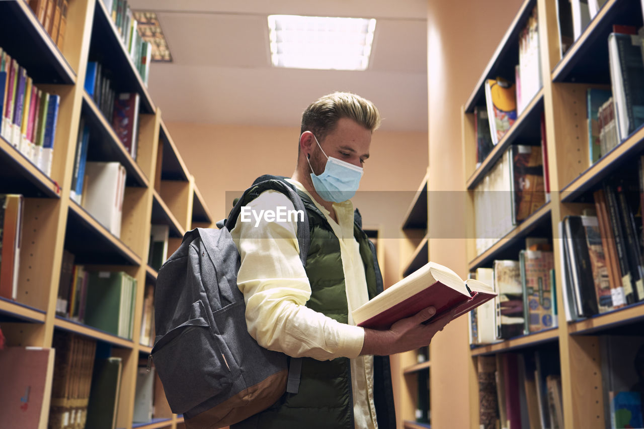 Young man with a mask is reading books in the university library