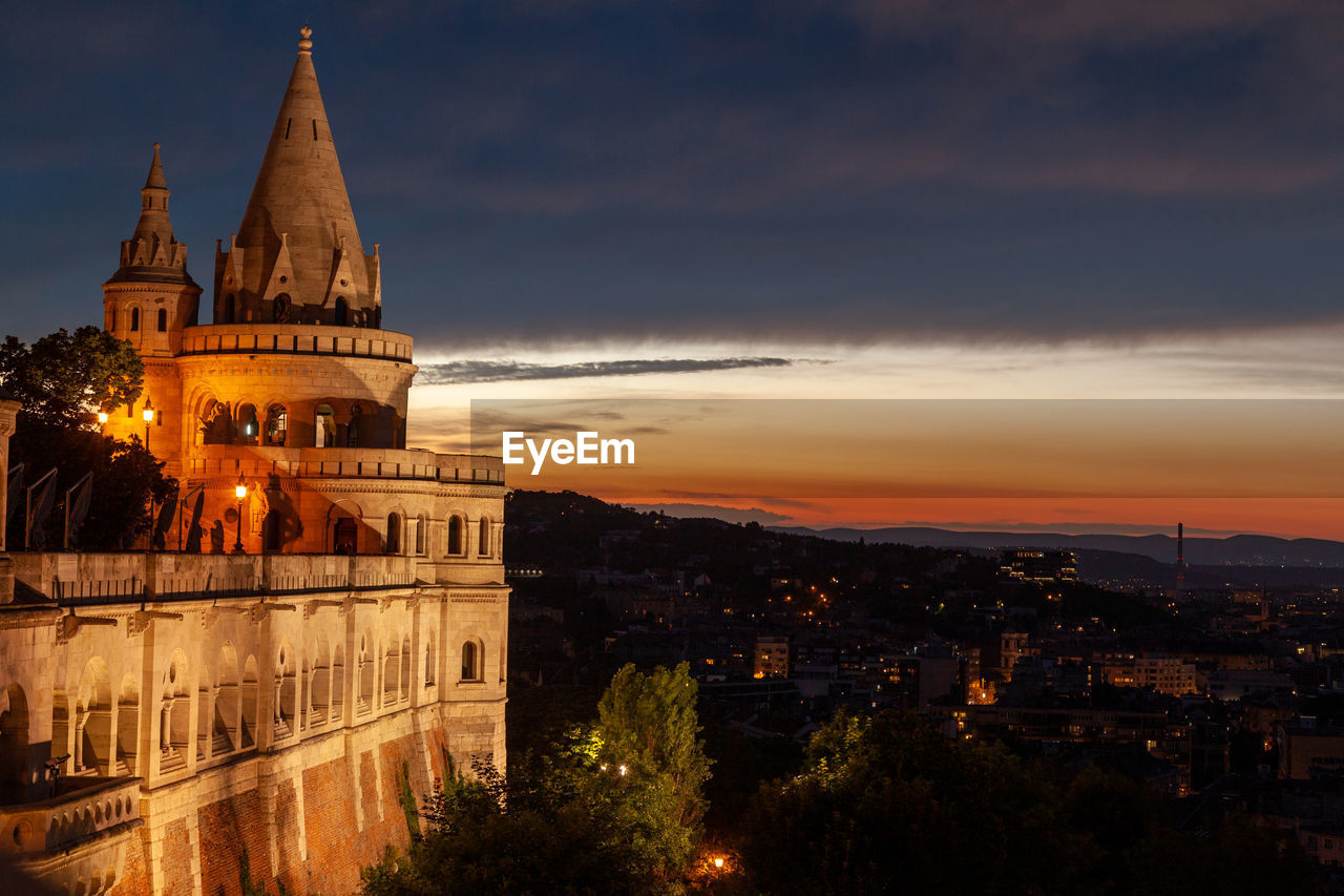 Illuminated buildings in city against sky during sunset
