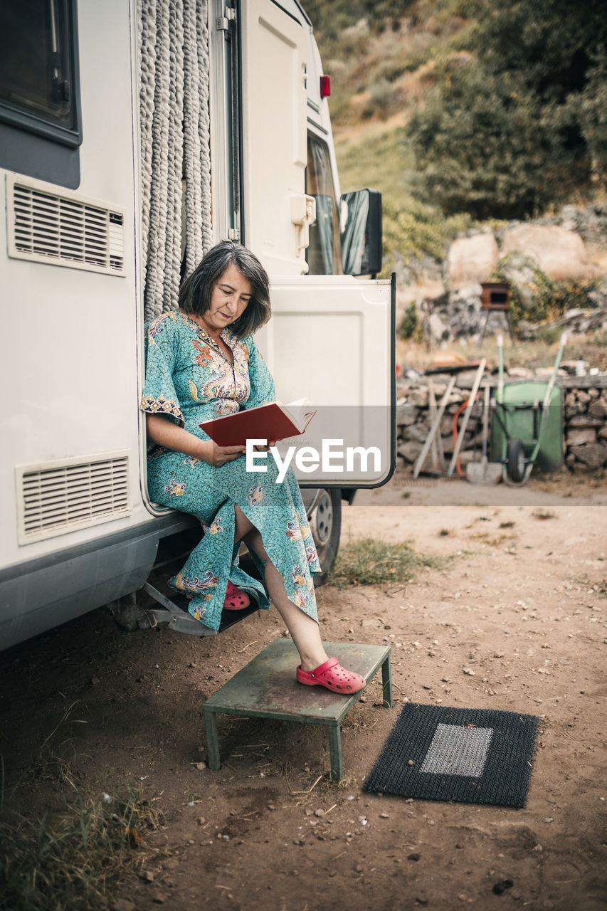 Woman reading book while sitting at camping van doorway