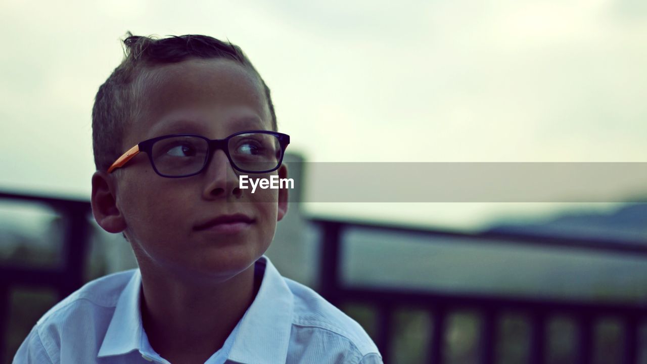 Thoughtful boy wearing eyeglasses against sky