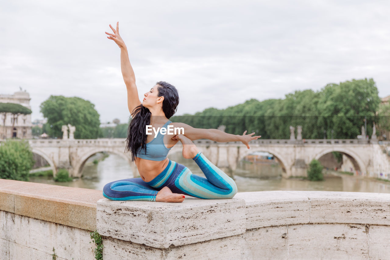 Full length of woman in yoga pose with arms raised against sky