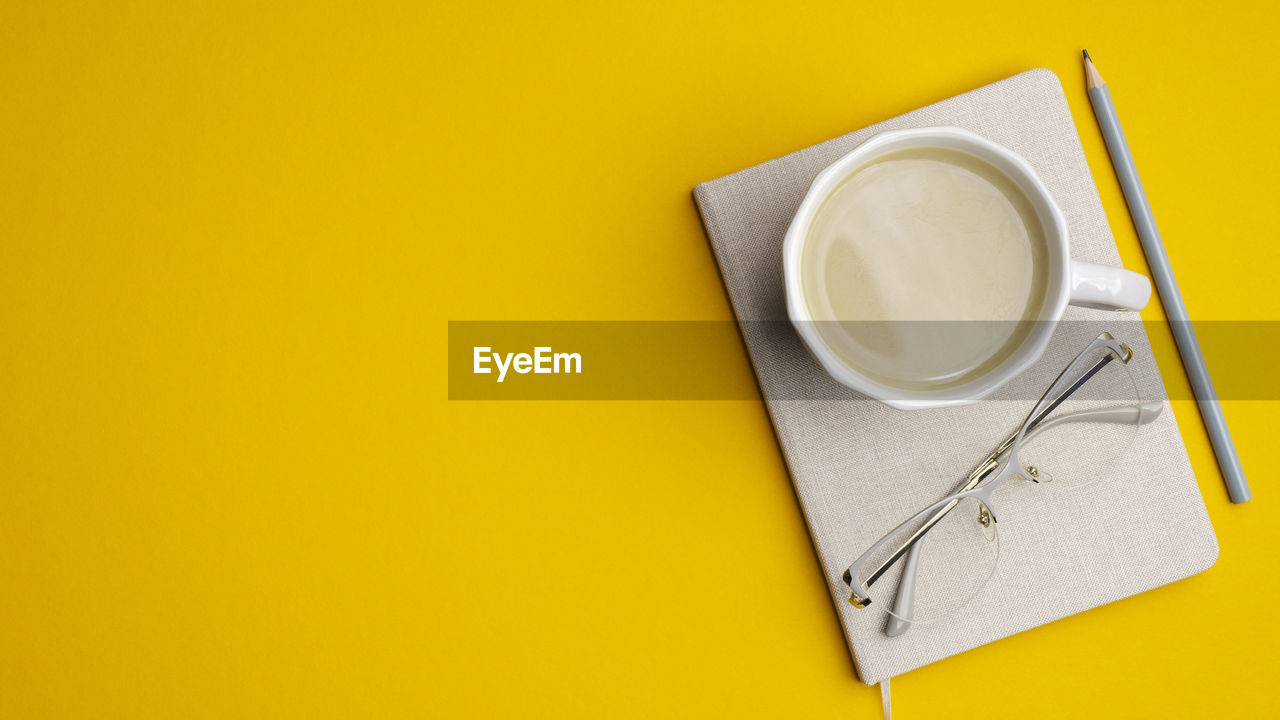 HIGH ANGLE VIEW OF COFFEE CUP ON TABLE AGAINST YELLOW WALL