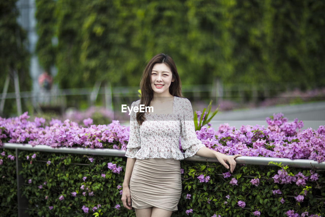 Portrait of smiling young woman standing by flowers at park