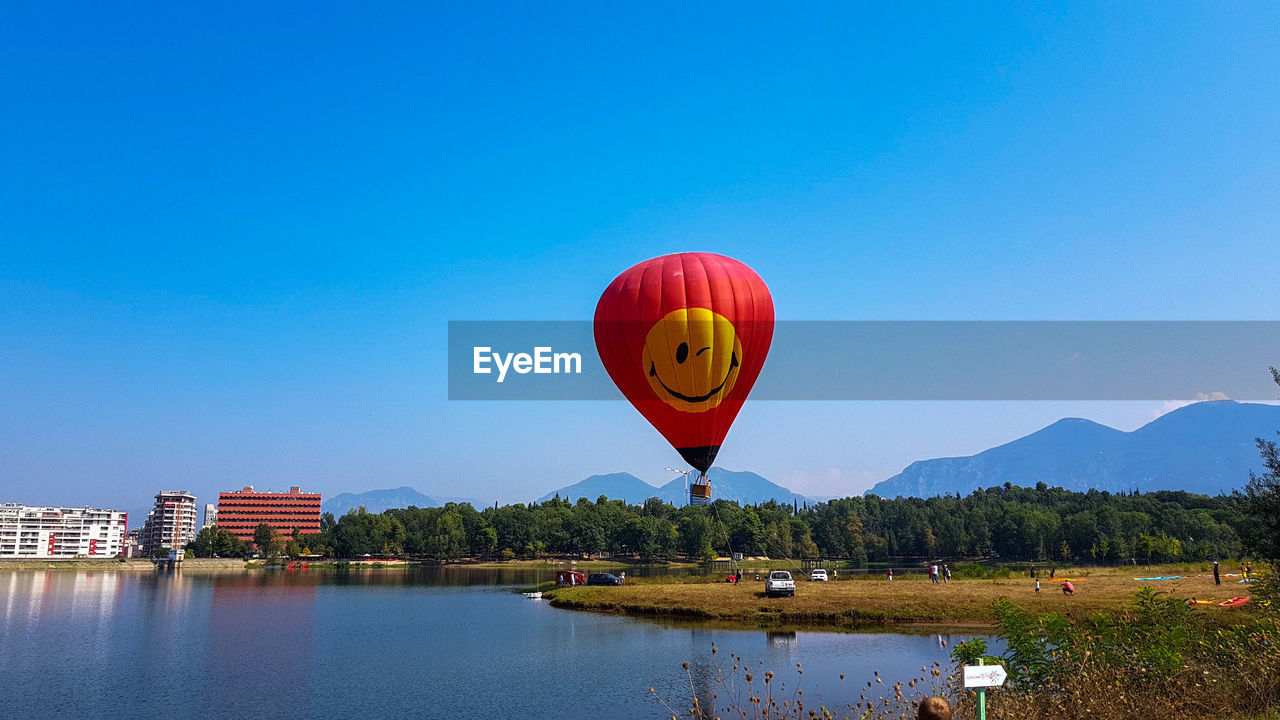 Red balloons flying over lake against clear blue sky