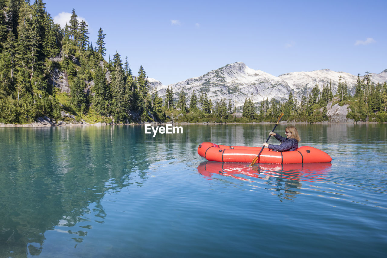 Retired woman paddling red boat on remote lake during a trip.