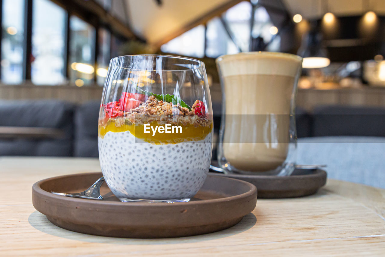 Chia pudding with mango puree, oats flakes and strawberries and cappuccino on table in cafe