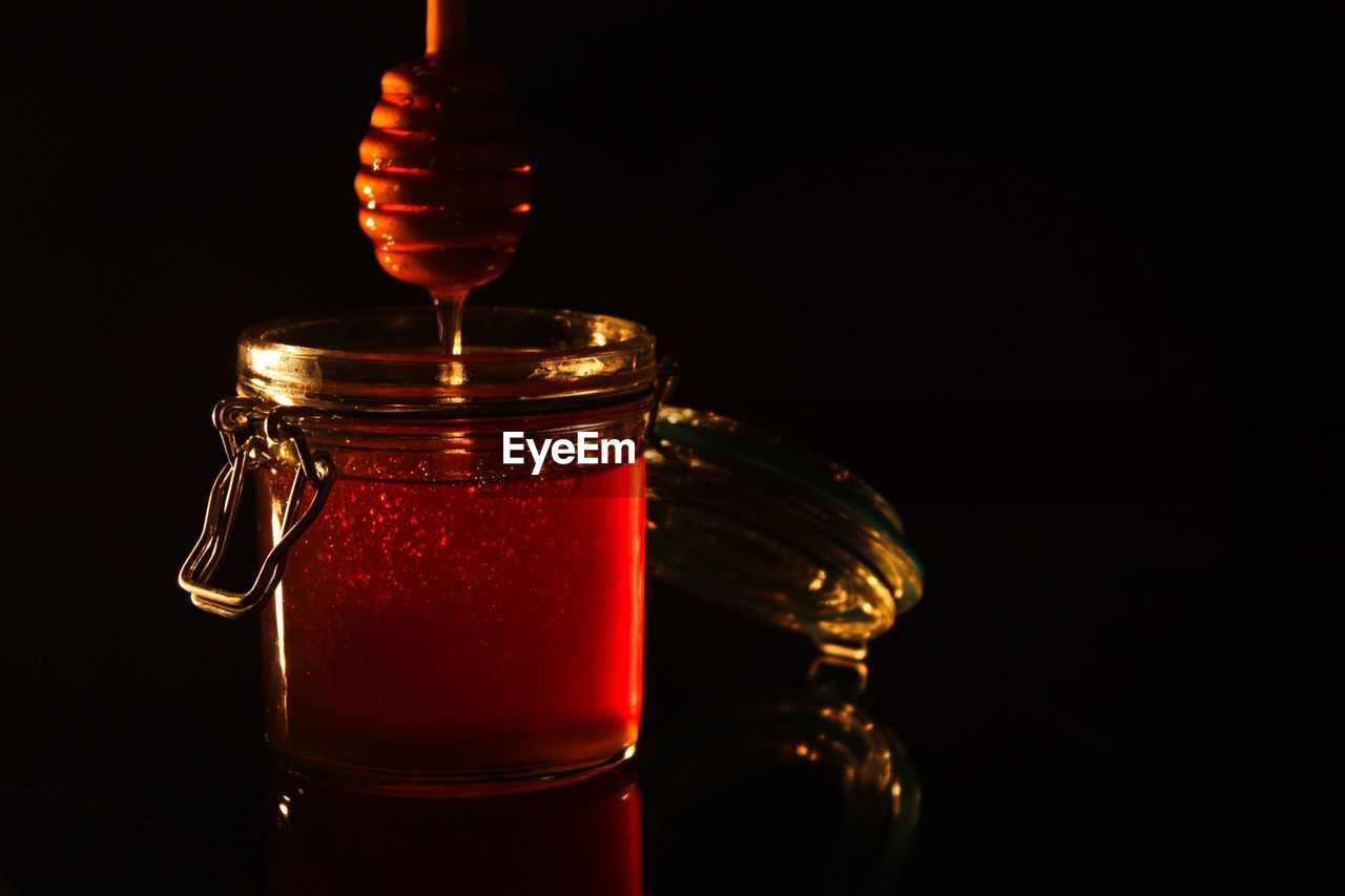 Close-up of honey in jar with dipper over black background