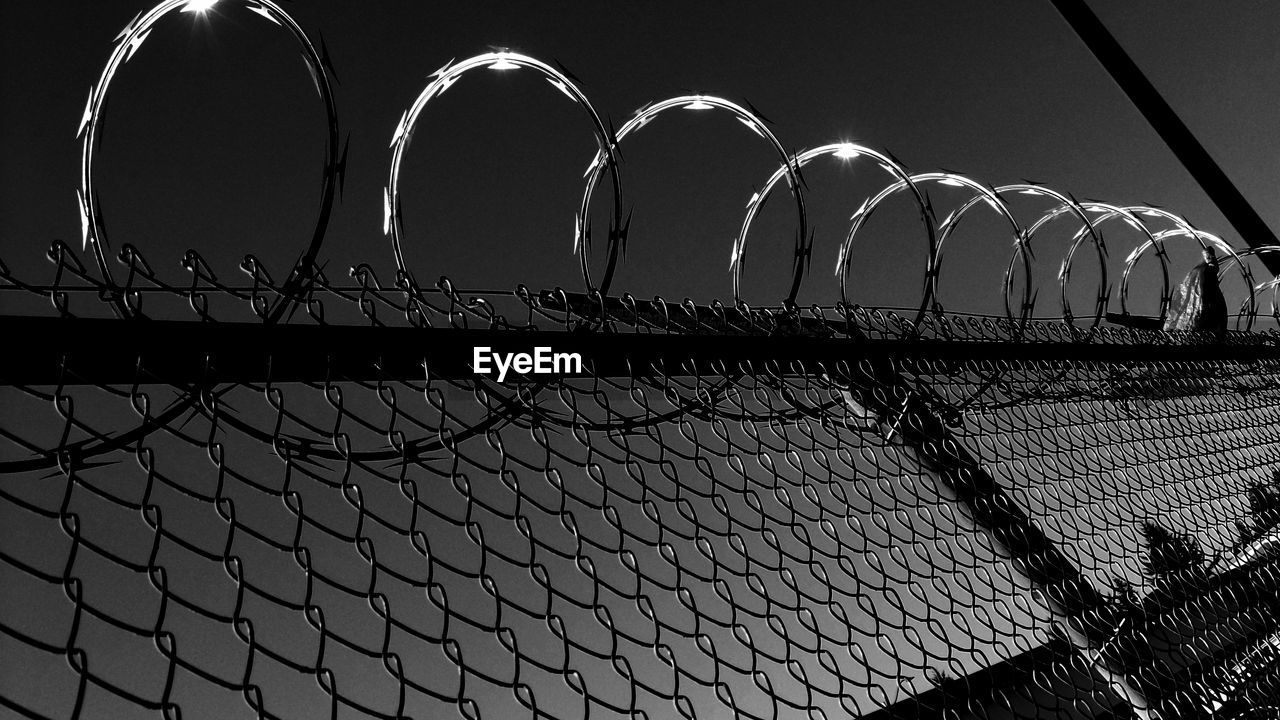 Low angle view of razor wire over chainlink fence against clear sky