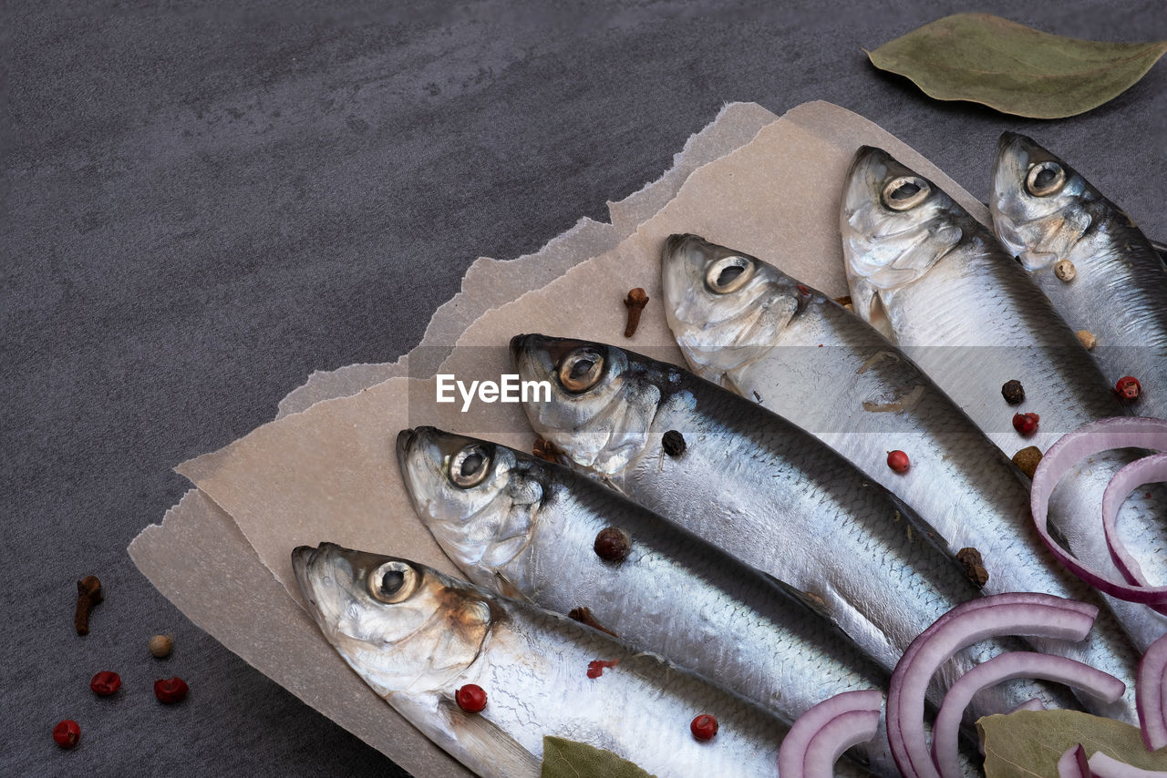 Close-up top view of several pickled herrings with spices on parchment paper on a serving board. 