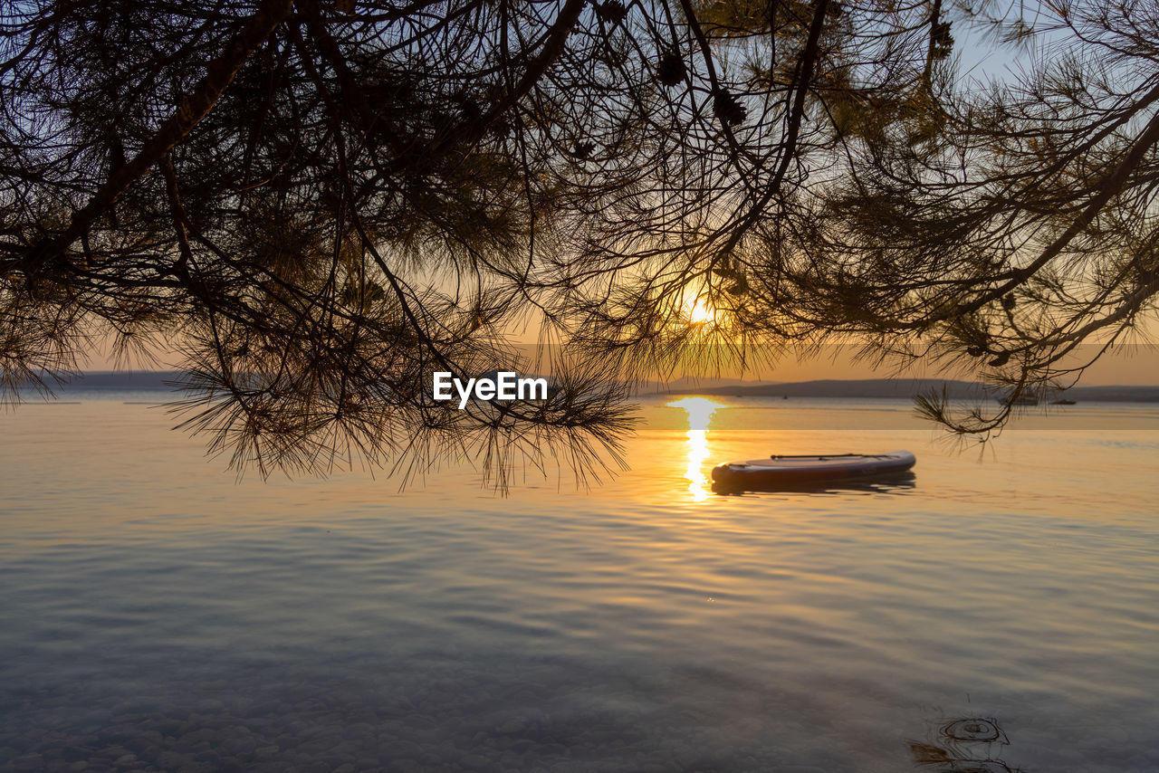 water, tree, reflection, sunset, sky, nature, beauty in nature, tranquility, scenics - nature, plant, tranquil scene, nautical vessel, lake, evening, transportation, mode of transportation, no people, dawn, branch, sunlight, outdoors, bare tree, silhouette, sun, idyllic, non-urban scene, waterfront, winter, orange color, shore, cloud, beach