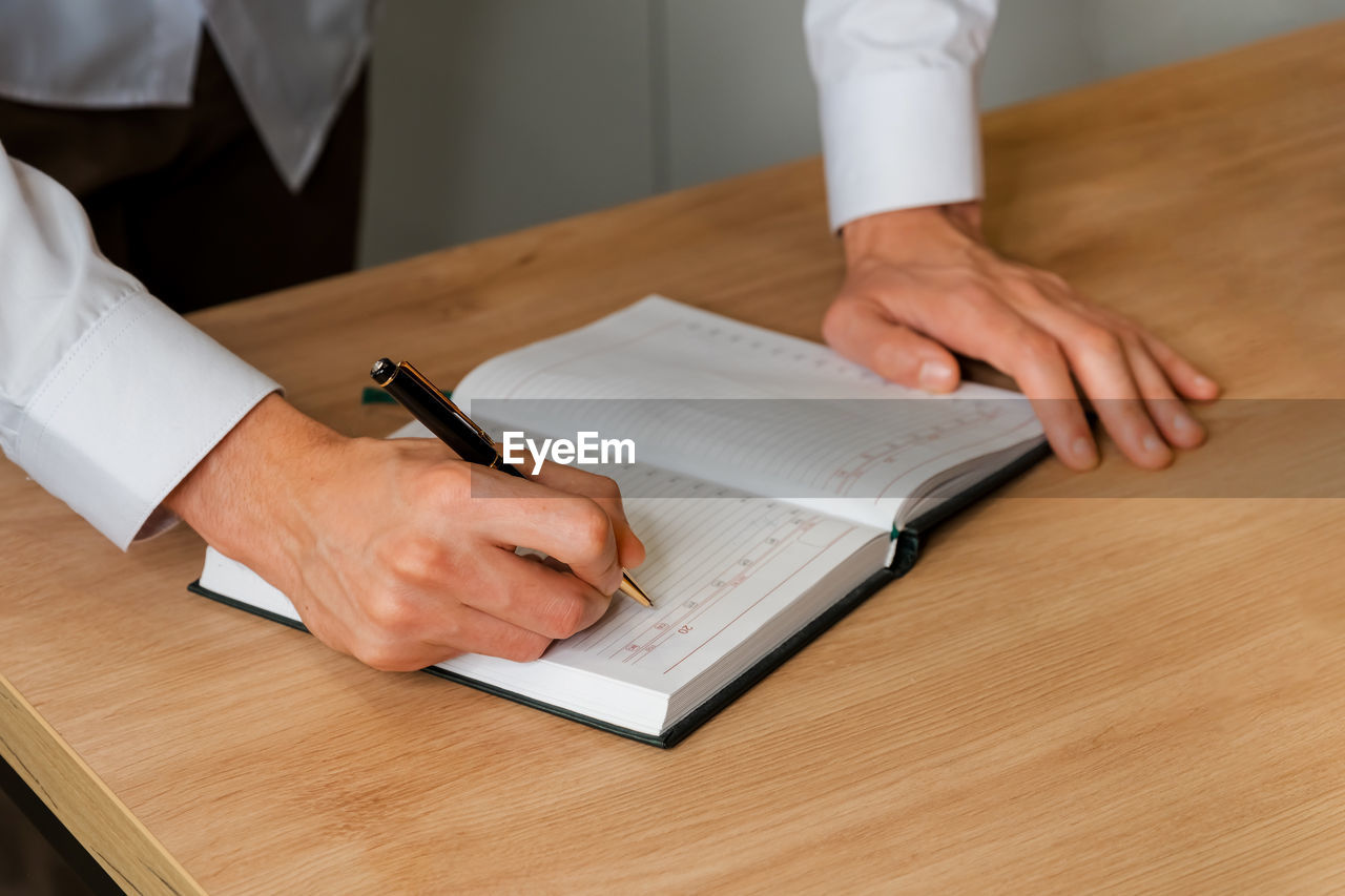 Young woman right hand writing plans on small diary with pen.