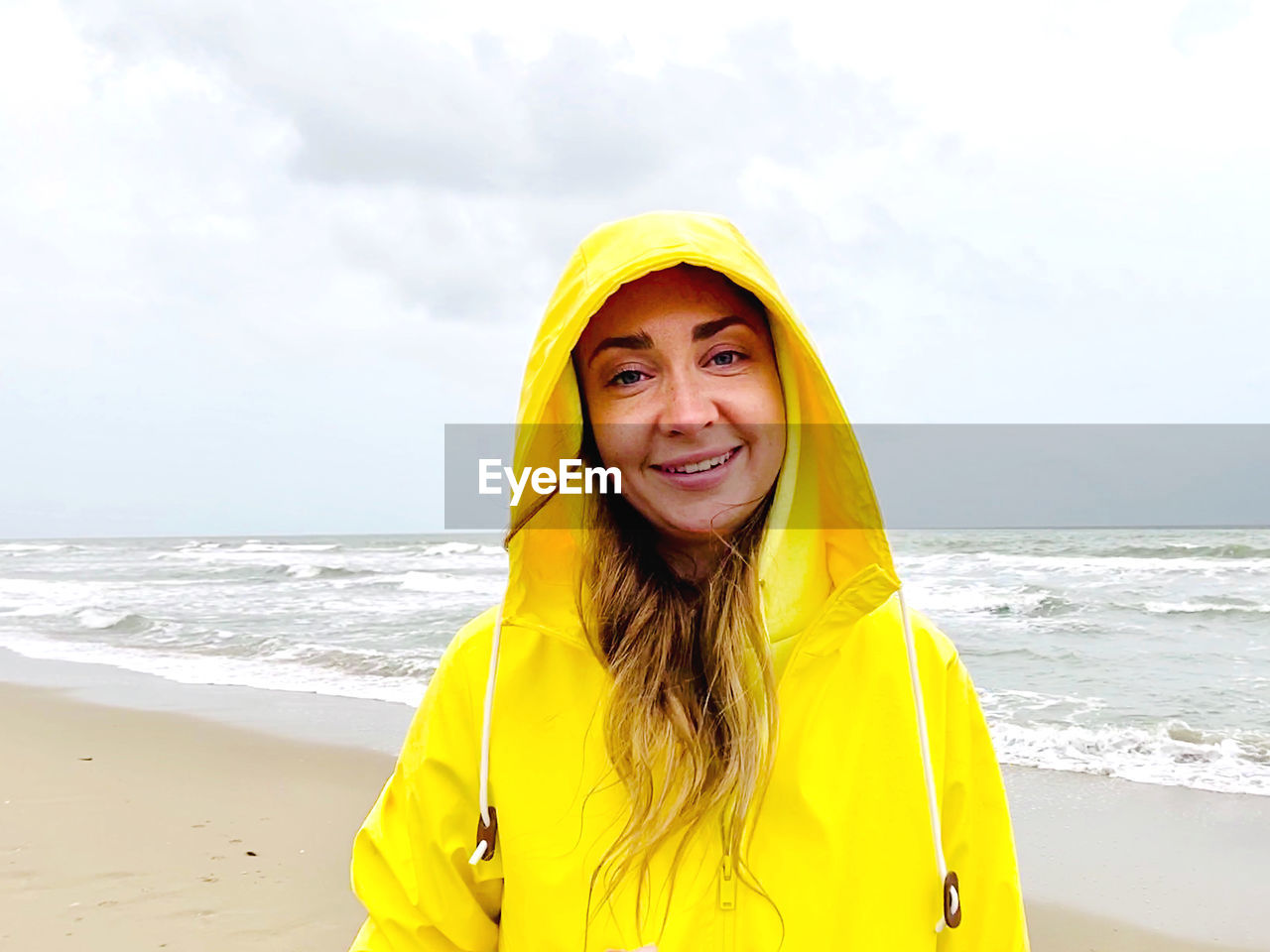 Portrait of smiling woman standing at beach against sky