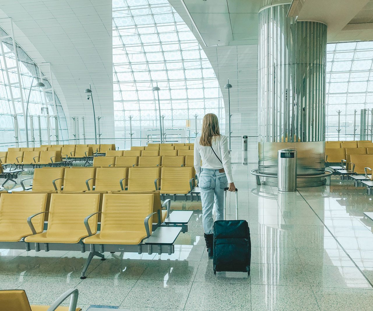 REAR VIEW OF WOMAN WITH UMBRELLA WALKING ON AIRPORT