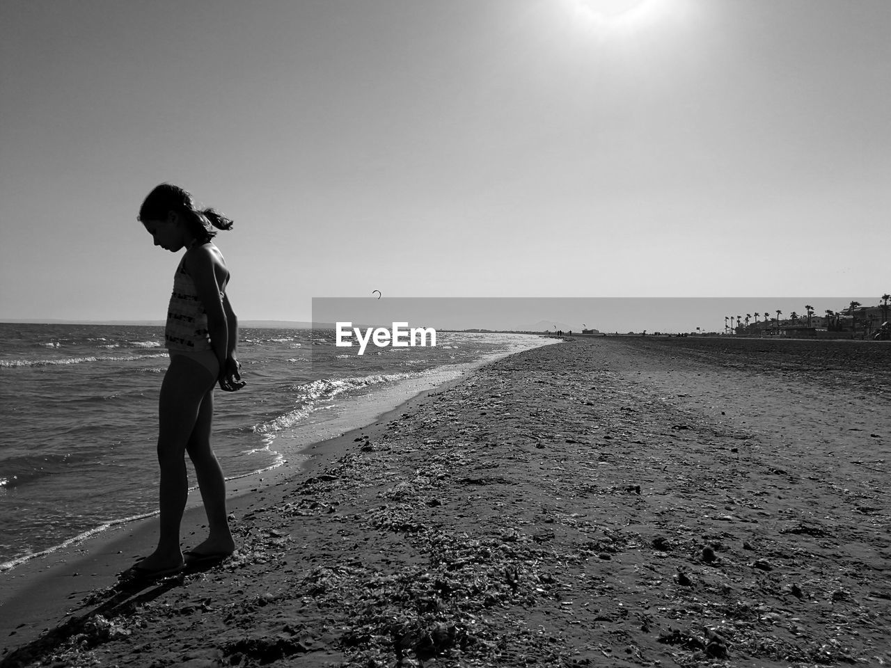 Side view of girl in swimsuit standing on shore at beach against clear sky