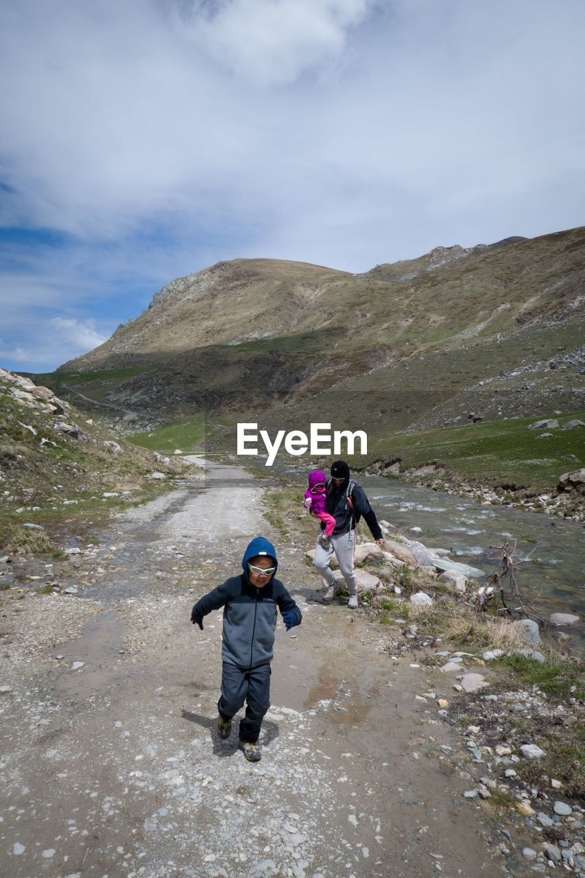 REAR VIEW OF PEOPLE ON MOUNTAIN ROAD AGAINST SKY