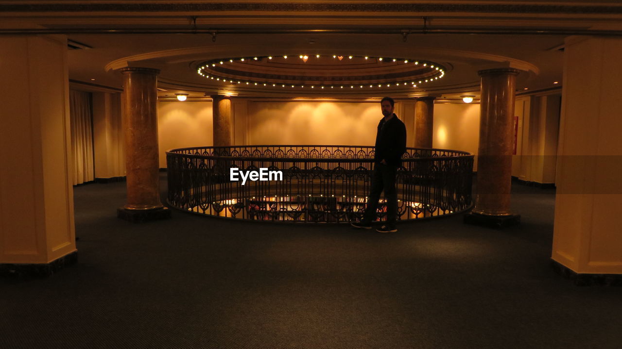 REAR VIEW OF MAN STANDING IN ILLUMINATED CORRIDOR OF BUILDING