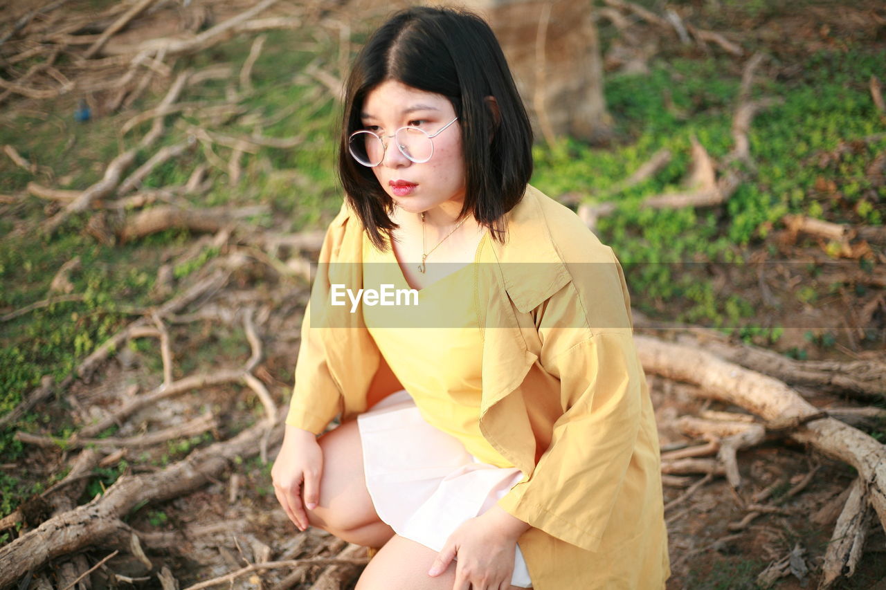 Young woman looking away while sitting on land