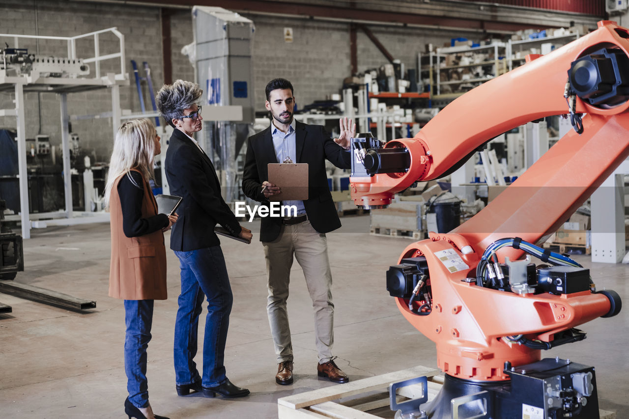 Businessman explaining colleagues over robotic arm at industry