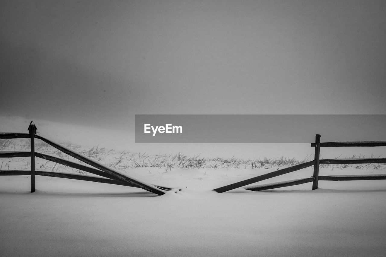 Fence on snow covered field against clear sky