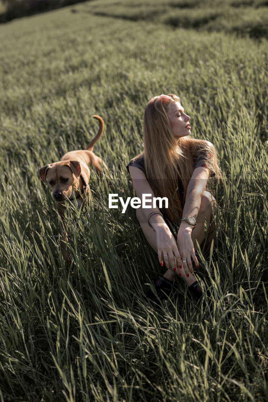 Young woman with dog sitting on grassy field