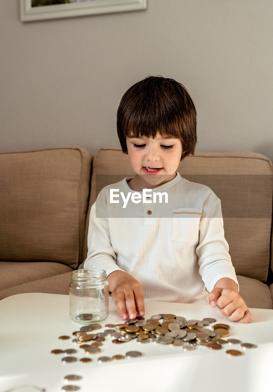 Happy little child counting coins putting them into glass jar. kid counting money saving from change 