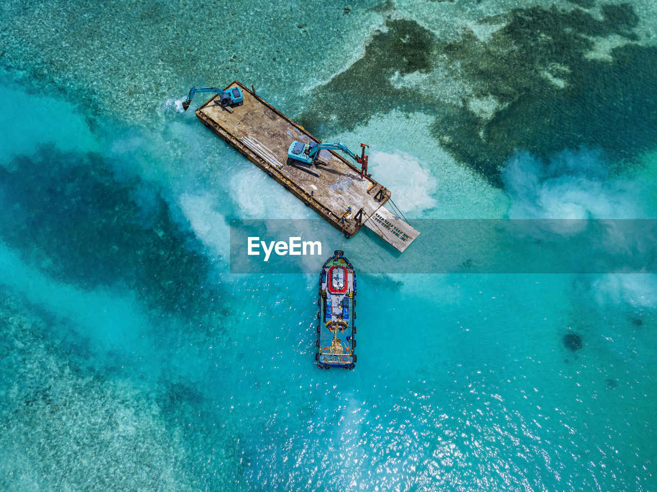 Aerial view of earth movers handling poles on floating platform in male atoll