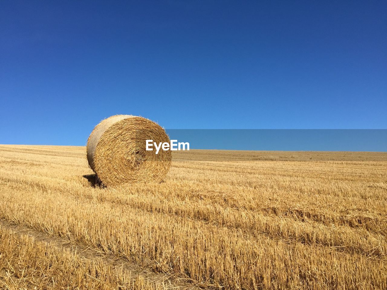 Hay bale on field against clear blue sky