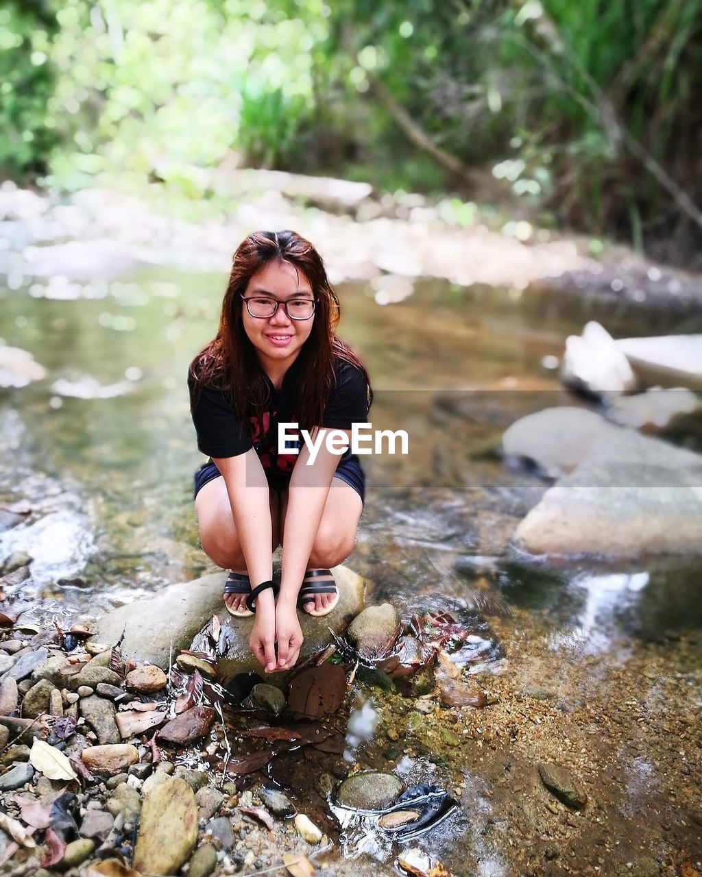 Portrait of young woman crouching on stone in stream at forest