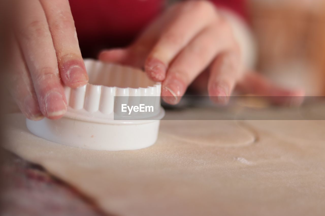 Cropped hands of woman cutting dough at home