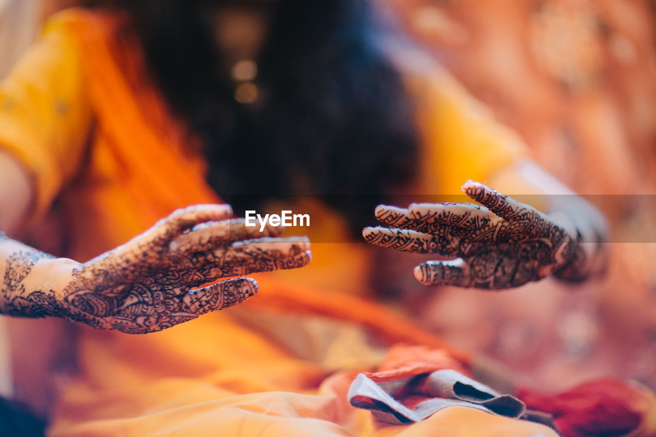 Midsection of woman with henna tattoo on hand sitting at home