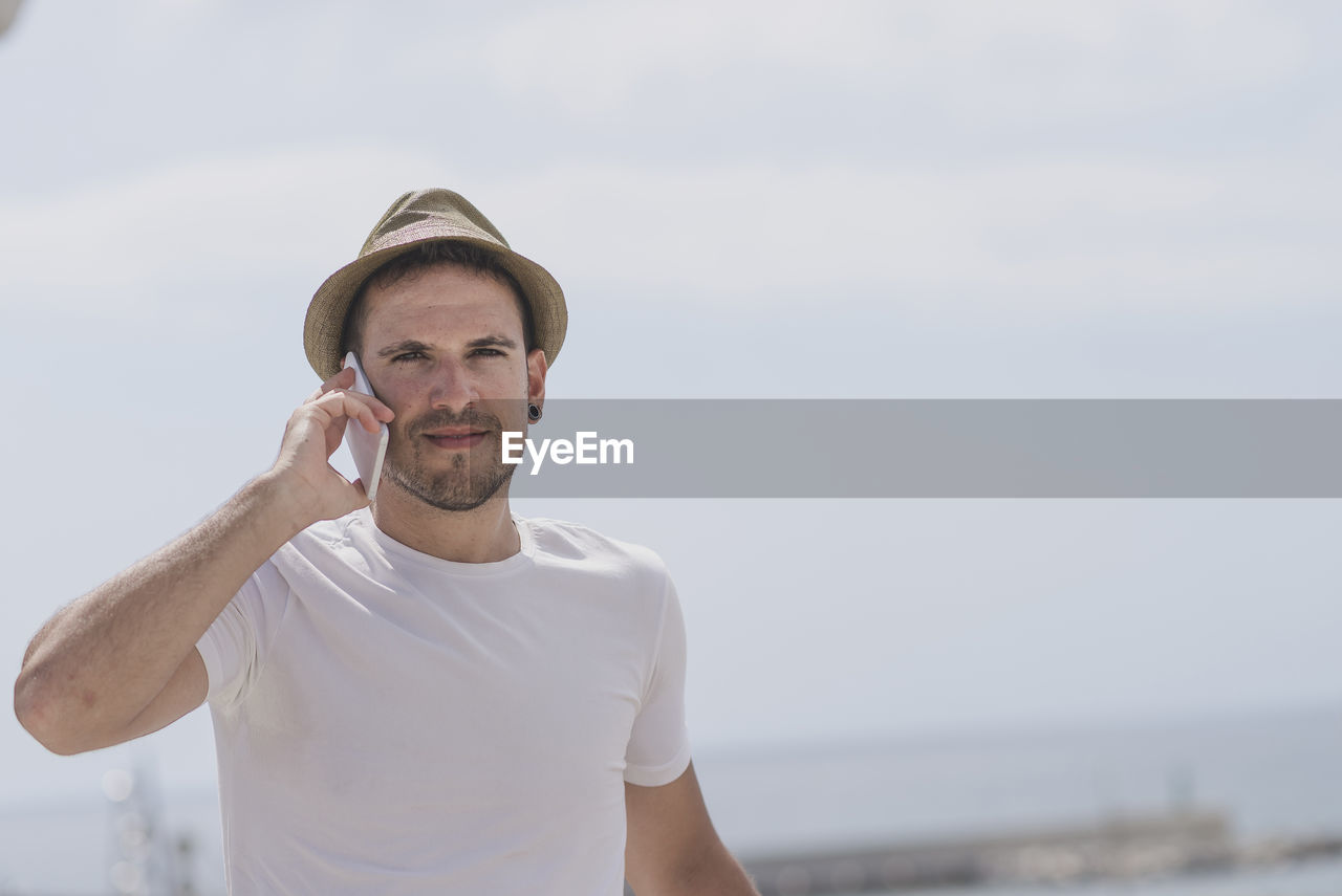 Portrait of smiling man using mobile phone while standing against sea at beach