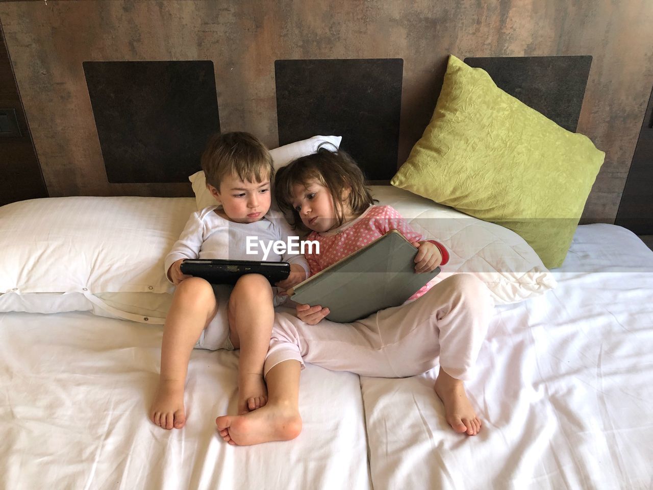Full length of boy and girl using digital tablet while lying on bed at home