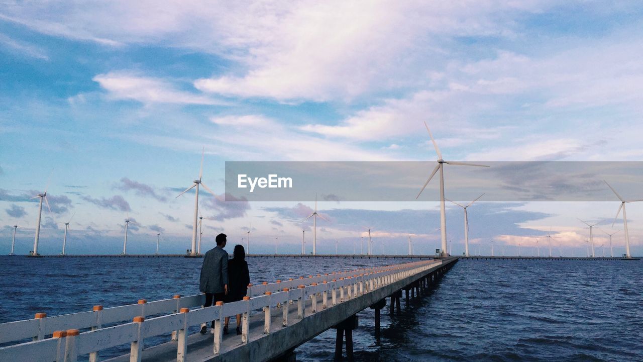 Couple walking on pier towards wind turbines
