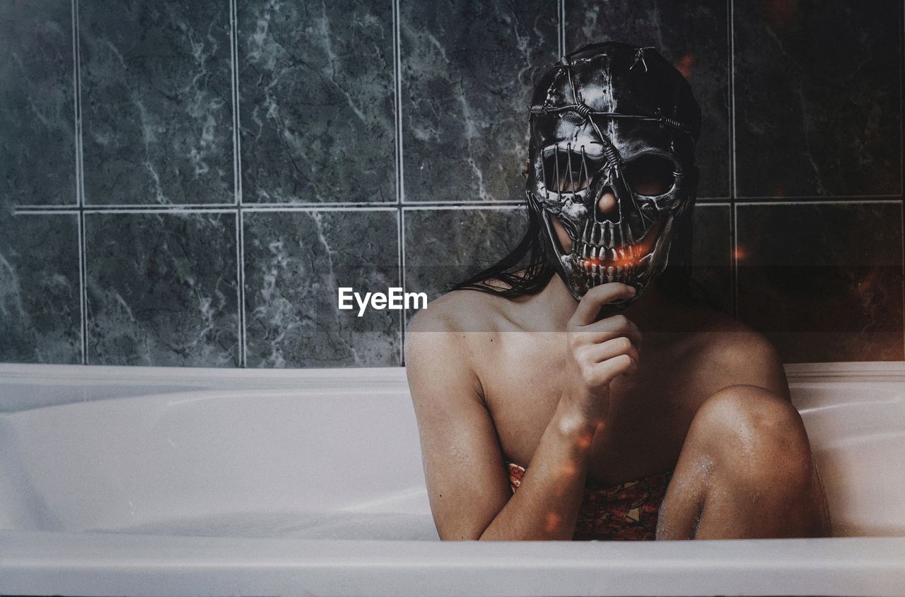 Woman wearing skull mask sitting in bathroom