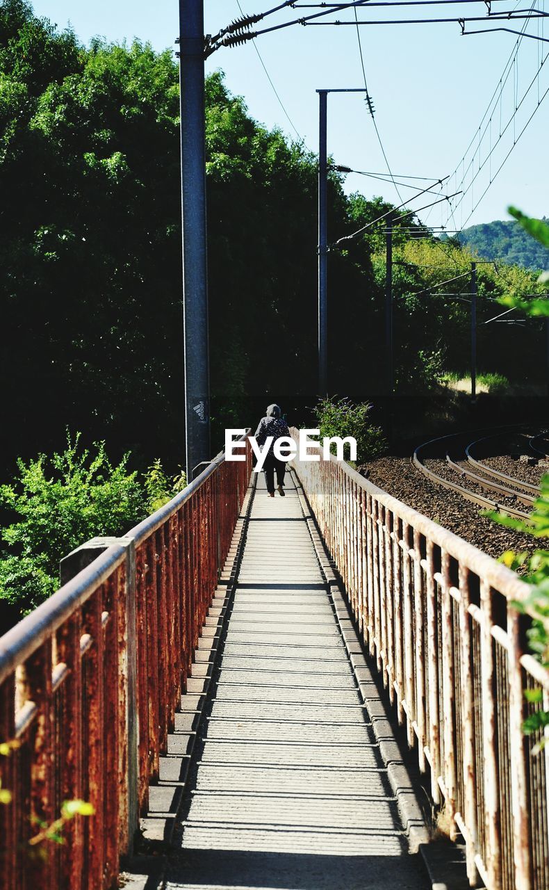 REAR VIEW OF WOMAN ON FOOTBRIDGE