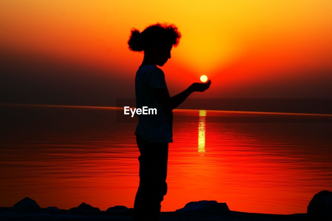 Silhouette girl standing against sea during sunset