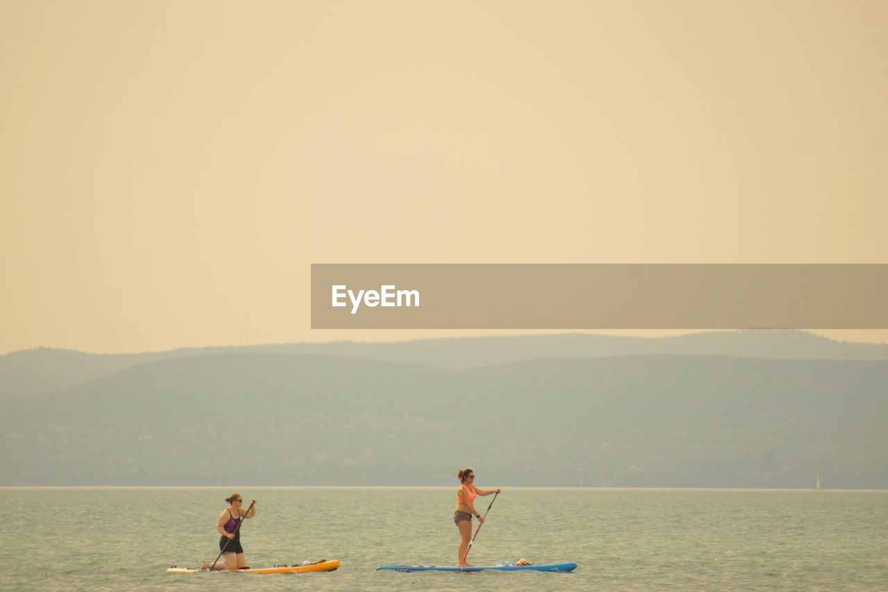 Women paddleboarding in sea against clear sky