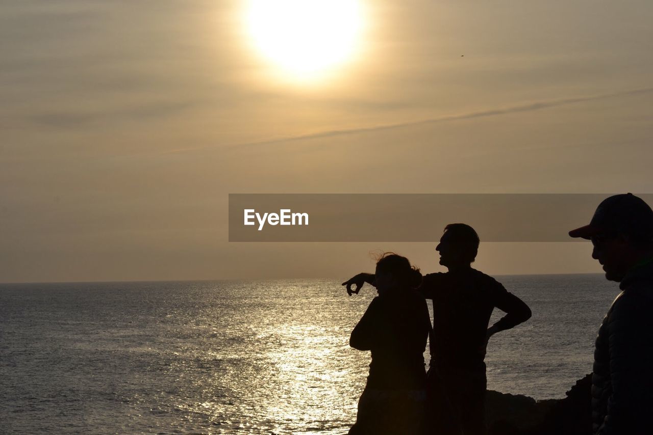 SILHOUETTE PEOPLE ON SEA AGAINST SKY AT SUNSET