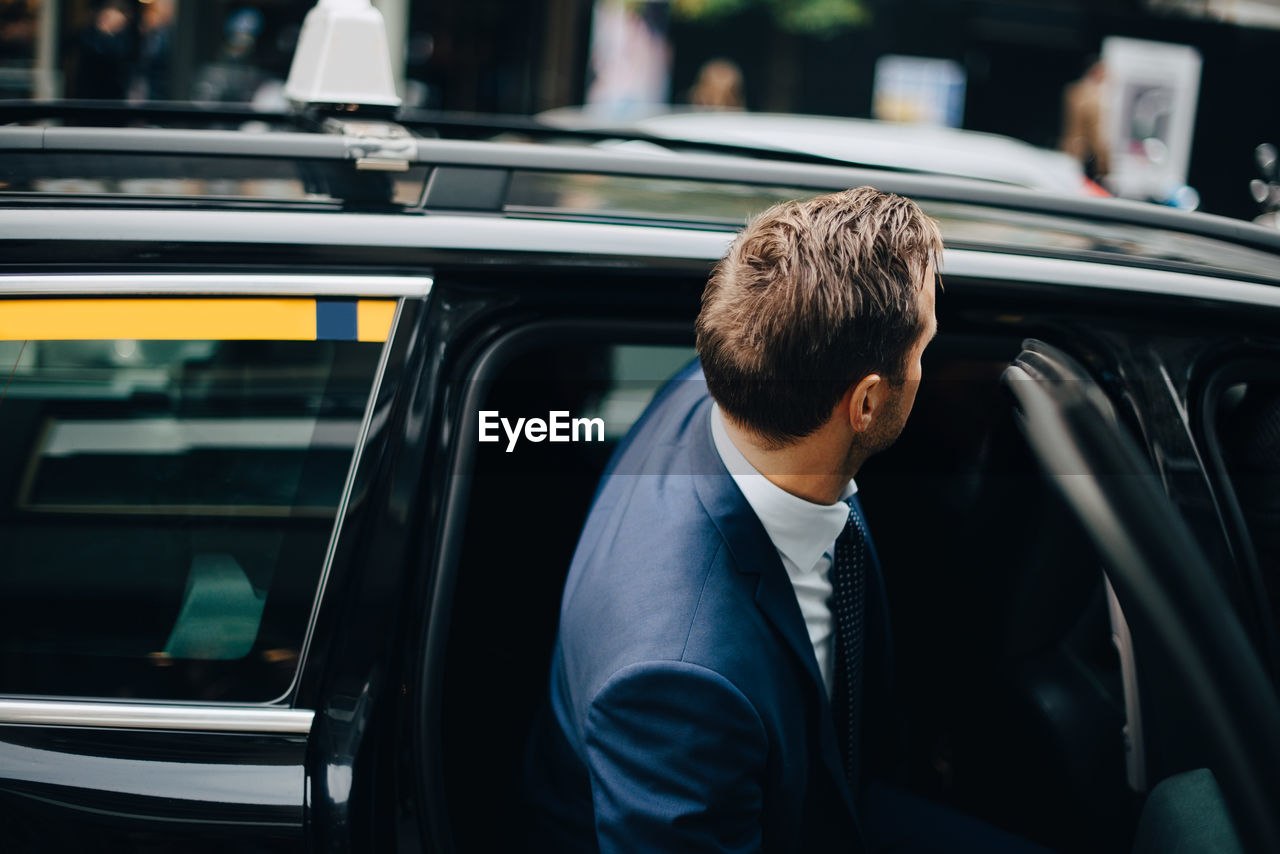 Side view of businessman entering taxi in city