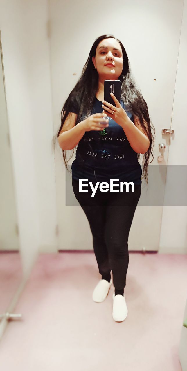 FULL LENGTH OF YOUNG WOMAN USING PHONE