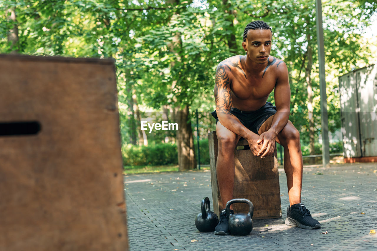 Full length of shirtless young man sitting in city