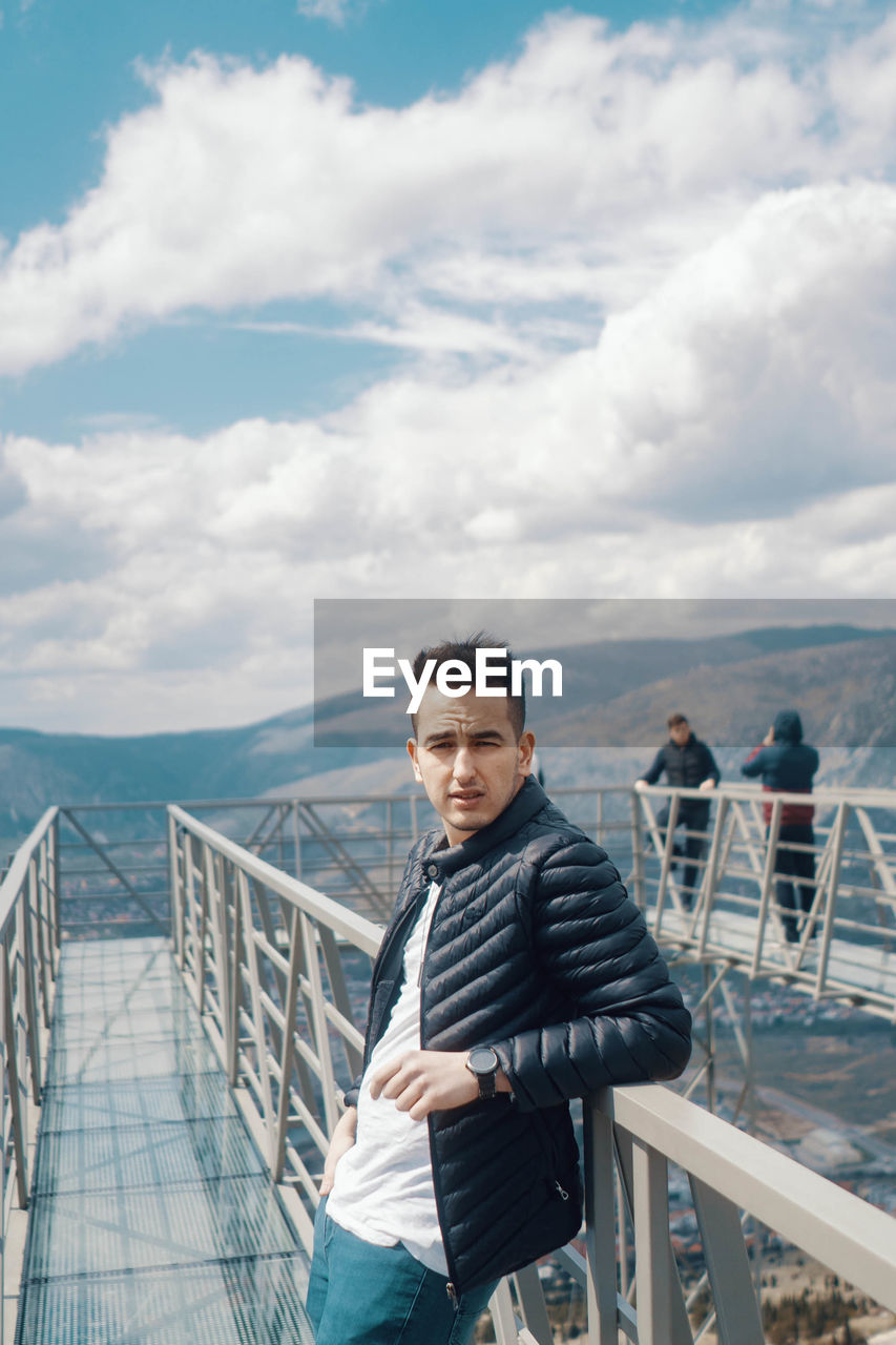 Portrait of young man standing on railing against sea