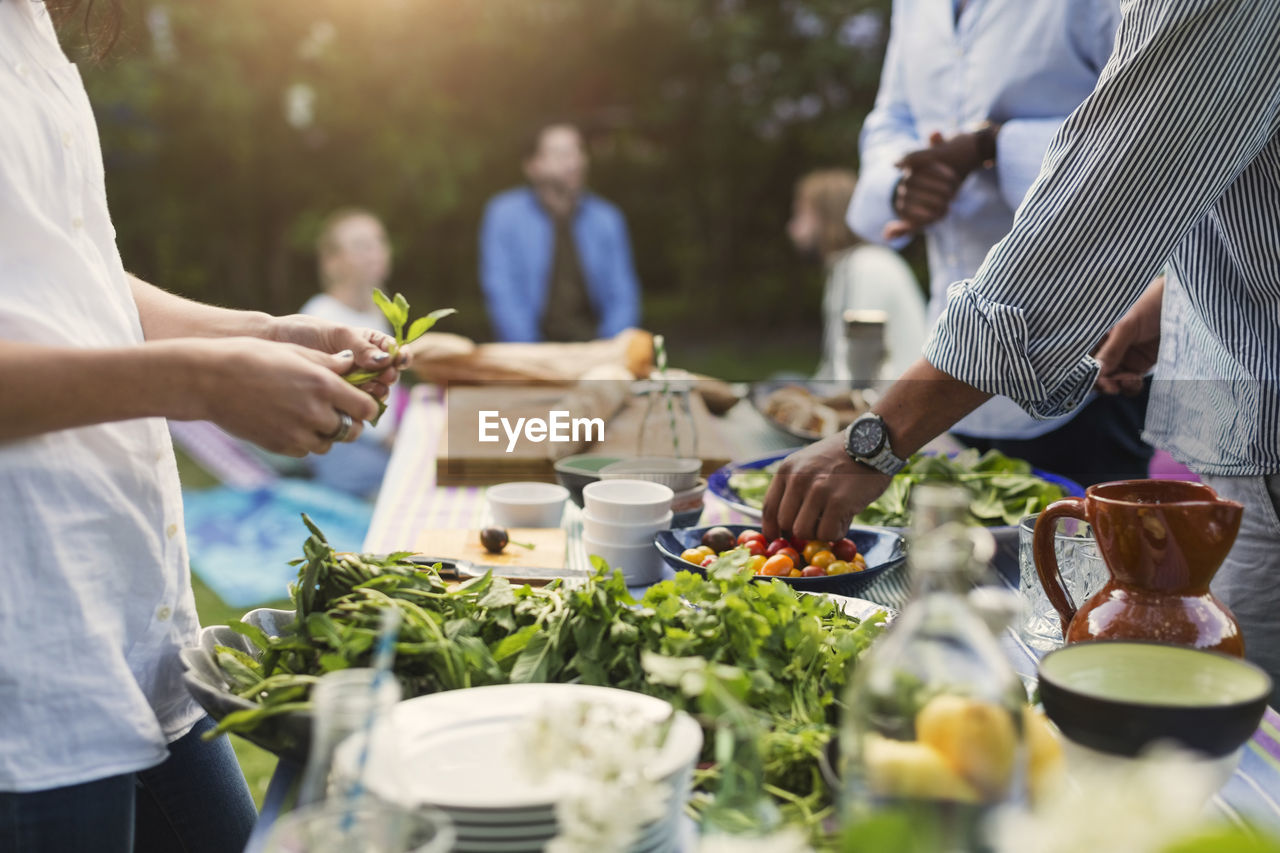 Midsection of friends preparing food at dining table in backyard