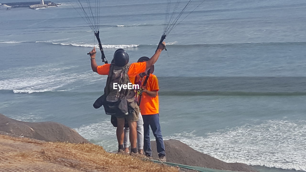 REAR VIEW OF MEN STANDING ON SHORE