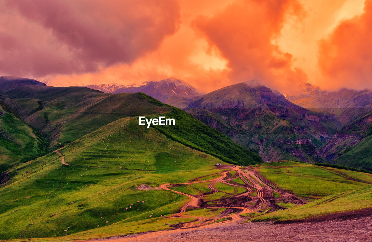 Scenic view of green mountains against dramatic sky during sunset