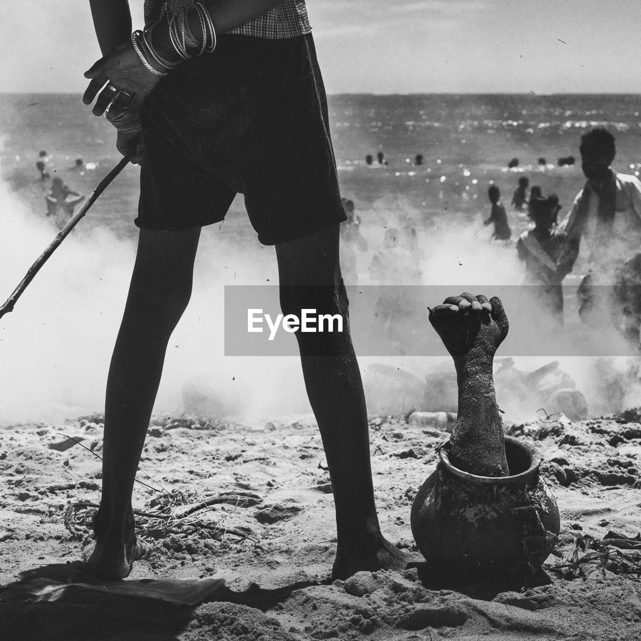 Low section of man standing by dead hand in pot at beach