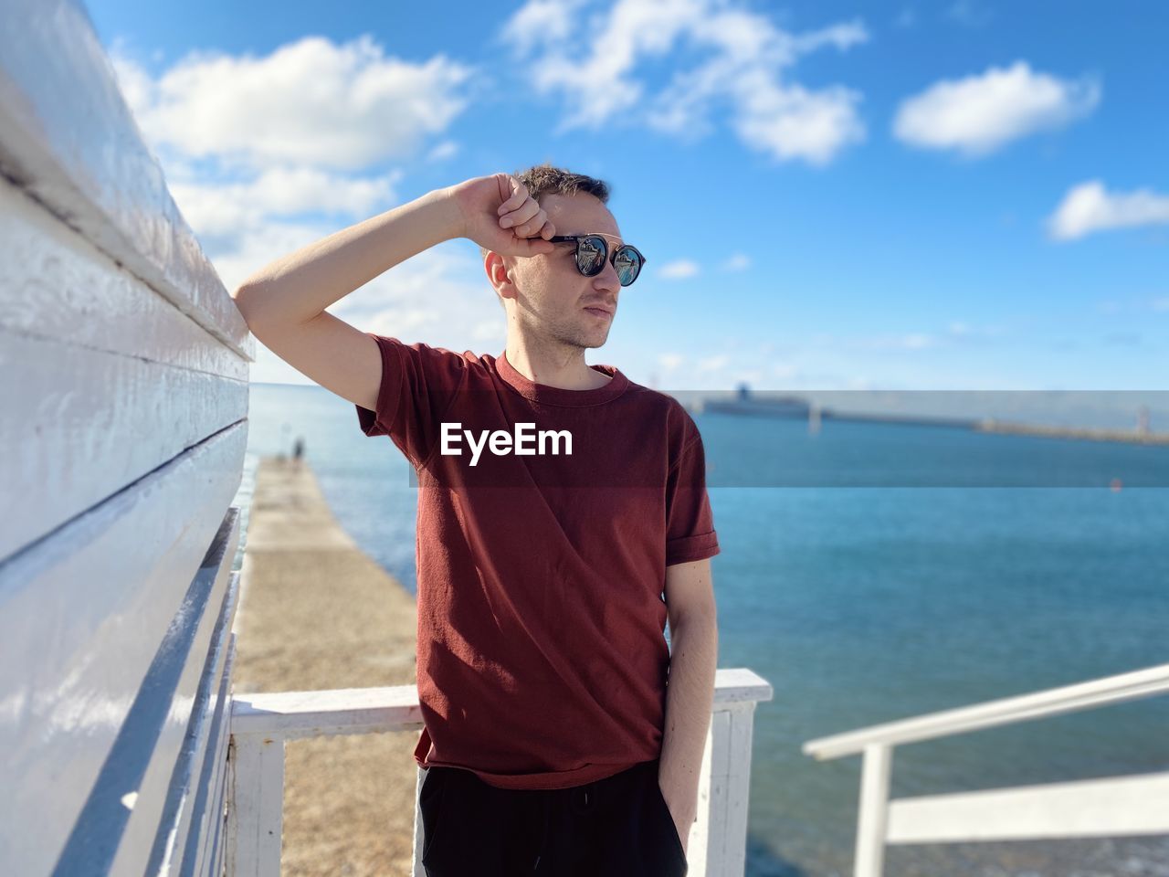 Man wearing sunglasses standing by railing against sea