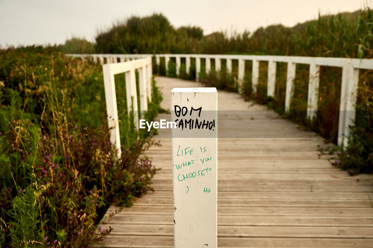 Close-up of wooden post with text on footbridge amidst plants 