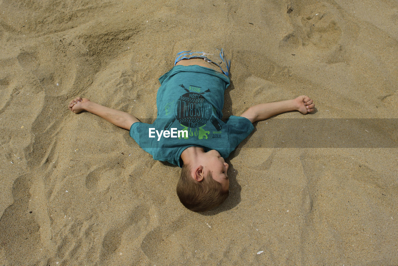 High angle view of boy buried in sand at beach