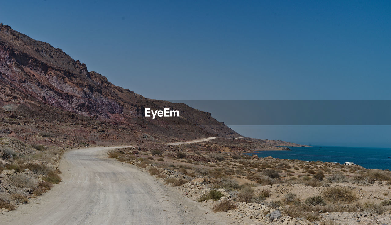 Scenic view of road by sea against clear blue sky